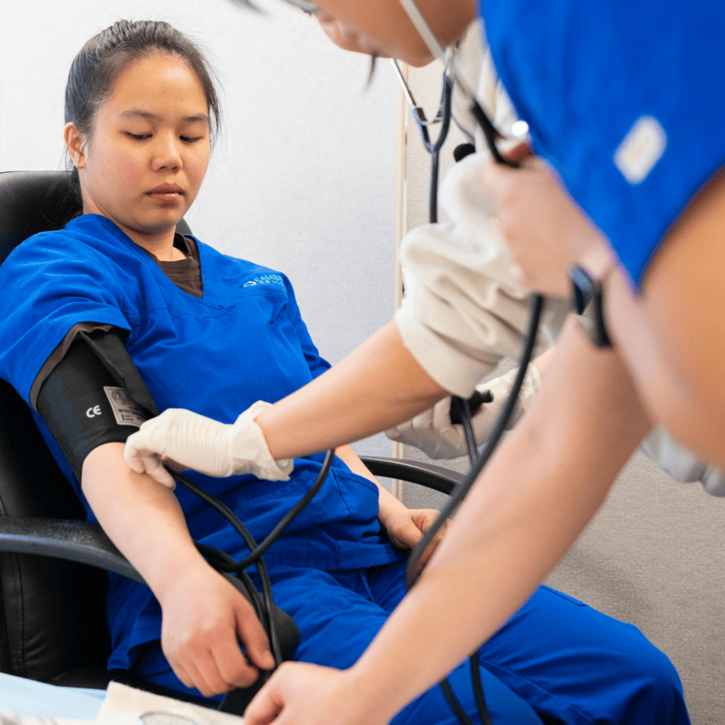 Healthcare student in blue scrubs practicing a blood pressure check on a classmate during clinical safety training